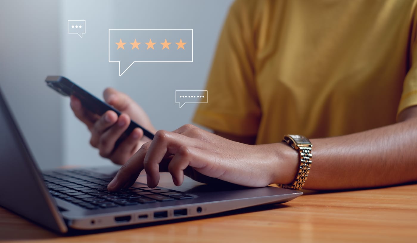 Personne tapant sur un ordinateur portable et tenant un smartphone, avec des icônes de chat et d'évaluation par étoiles